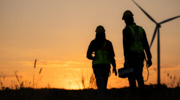 Silhouette of workers at sunset walking near a wind turbine.